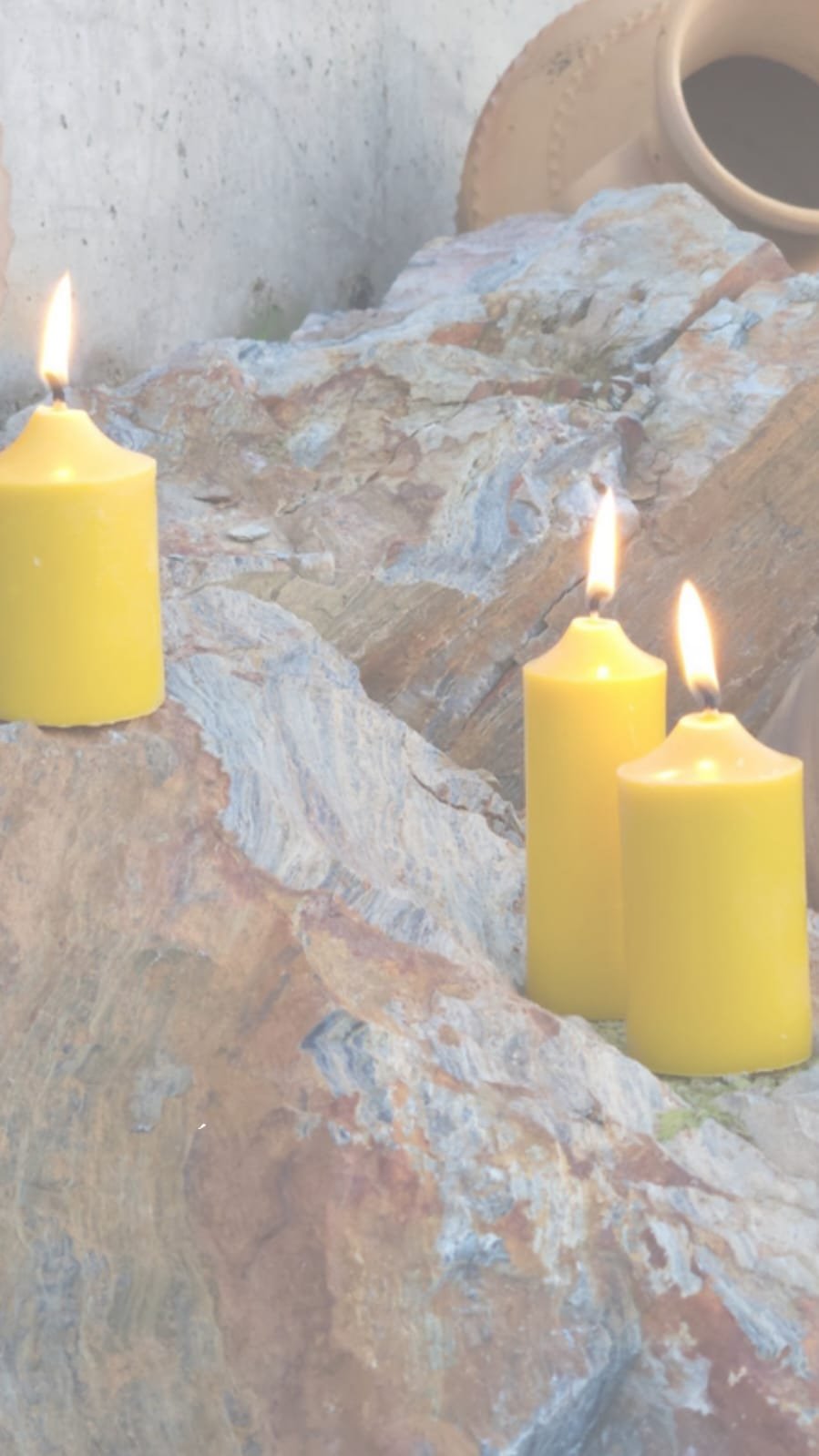 Inicio Tres velas de cera de abeja encendidas sobre una roca, junto a una vasija de barro
